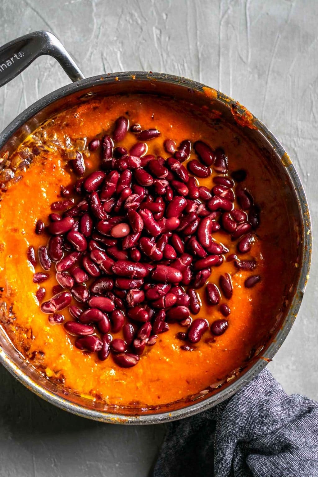 Making the afghan kidney bean curry. In a pot we have added the broth and spiced tomato sauce to the caramelized onions and have piled the kidney beans on top of that. 