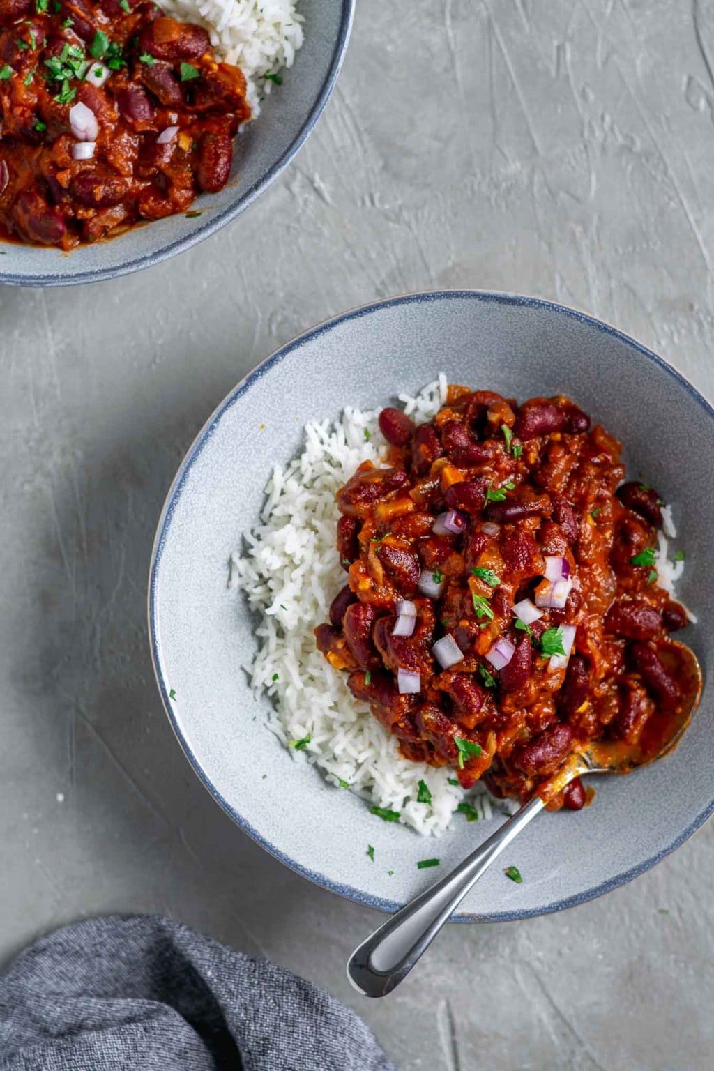 Afghan Kidney bean curry (lubya) is served in a bowl atop basmati rice and garnished with cilantro and minced red onion.