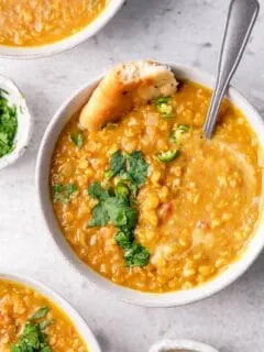 soup served in a bowl garnished with cilantro, green chilies, and garlic naan