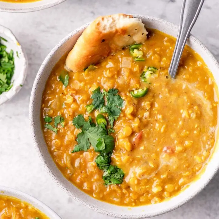 soup served in a bowl garnished with cilantro, green chilies, and garlic naan