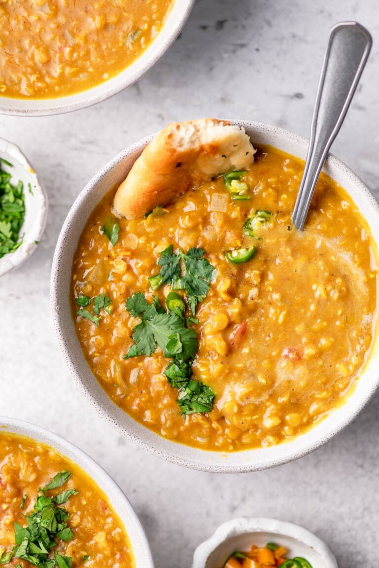 soup served in a bowl garnished with cilantro, green chilies, and garlic naan