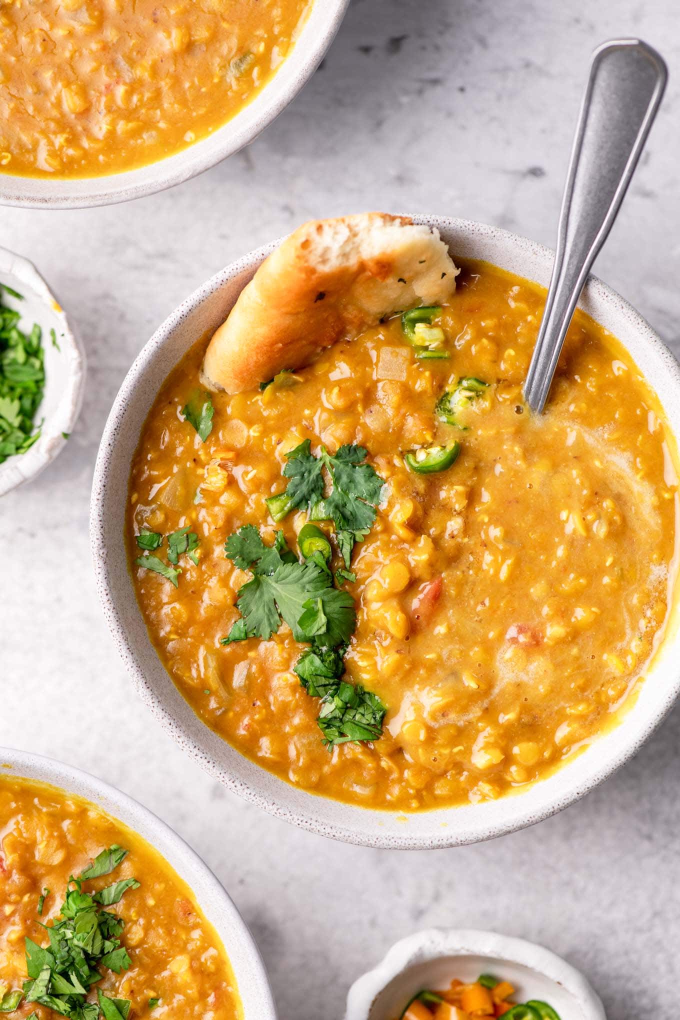 soup served in a bowl garnished with cilantro, green chilies, and garlic naan