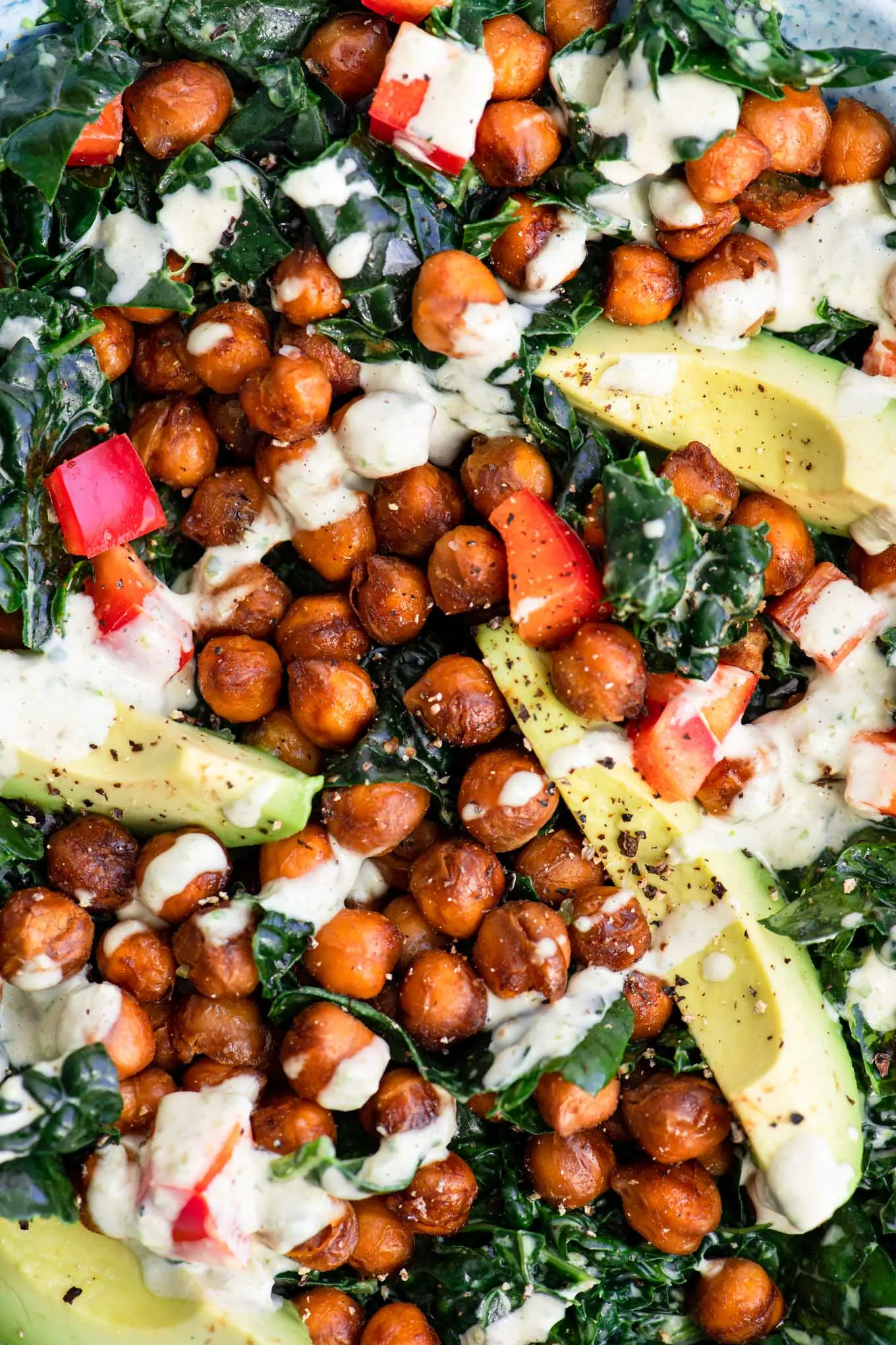 close up of kale salad with creamy roasted jalapeño tahini dressing, topped with smoky chickpeas, red bell pepper, and avocado