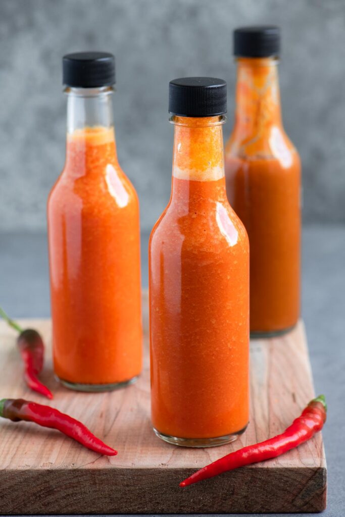 bottled homemade hot sauce on a cutting board with 3 red chilies