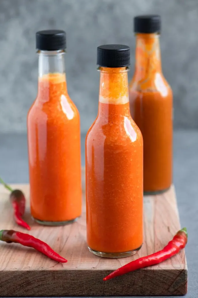 bottled homemade hot sauce on a cutting board with 3 red chilies