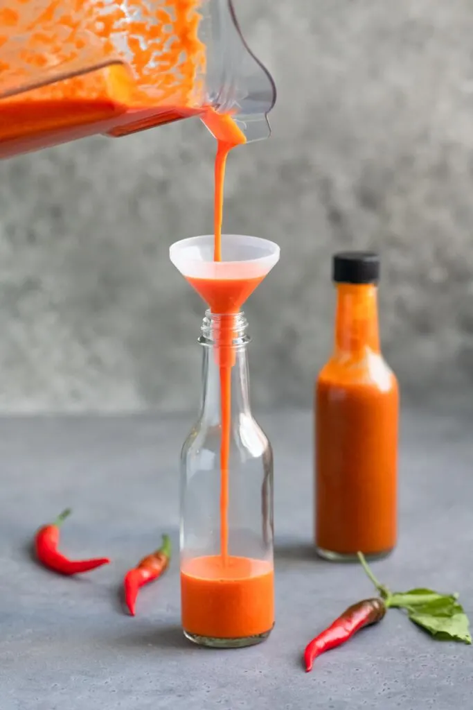 pouring hot sauce into a bottle with a small funnel