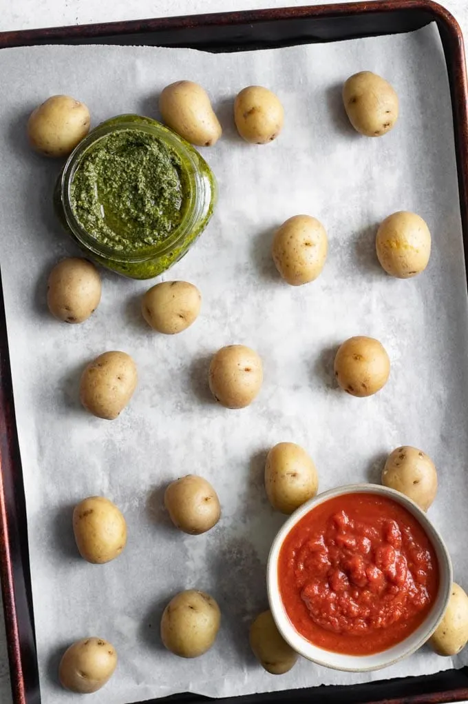 baby potatoes boiled and ready to be smashed on a baking sheet. Bowls of pesto and tomato sauce in photo.