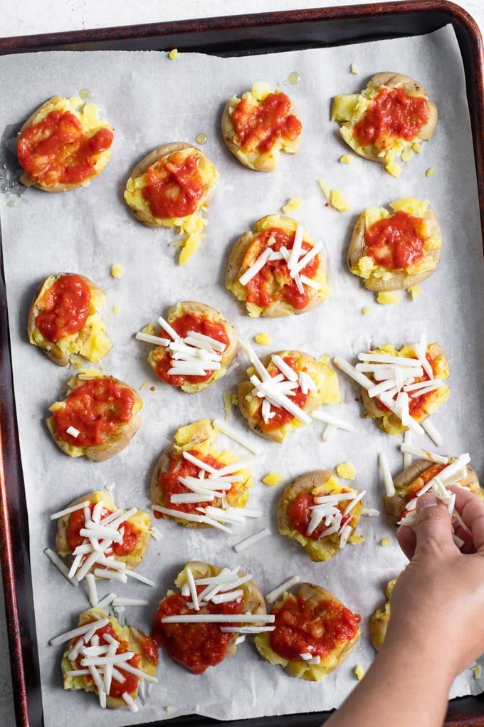 baby potatoes smashed and being topped with tomato sauce and vegan mozzarella