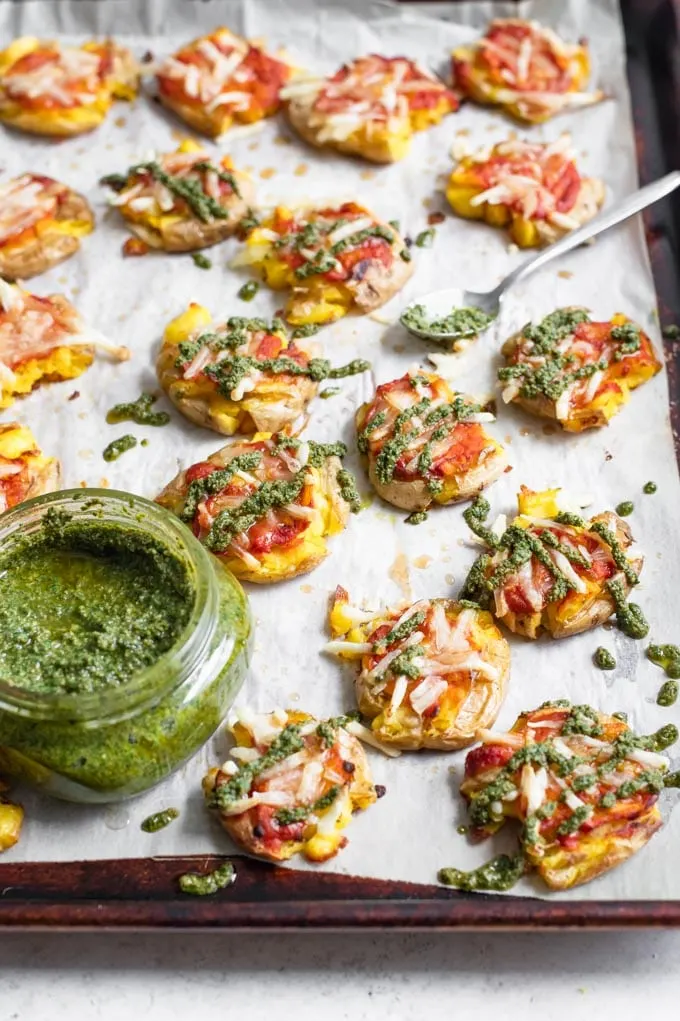 drizzling pesto overtop the smashed potatoes, which are on the baking tray