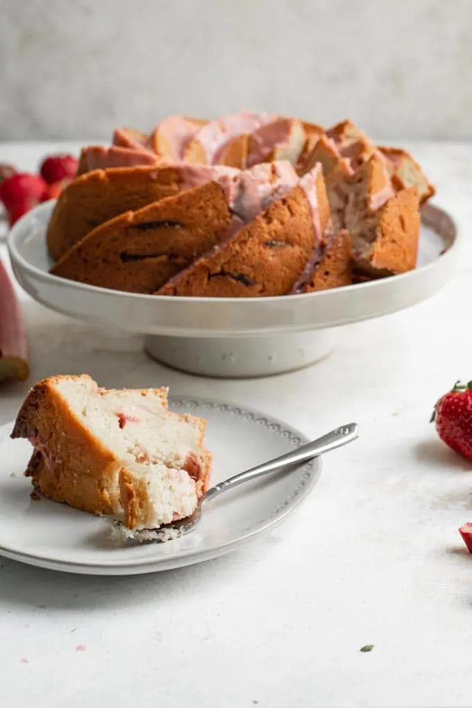 a close up of a slice of the almond rhubarb bundt cake with a forkful cut off the slice and the rest of the cake in the background