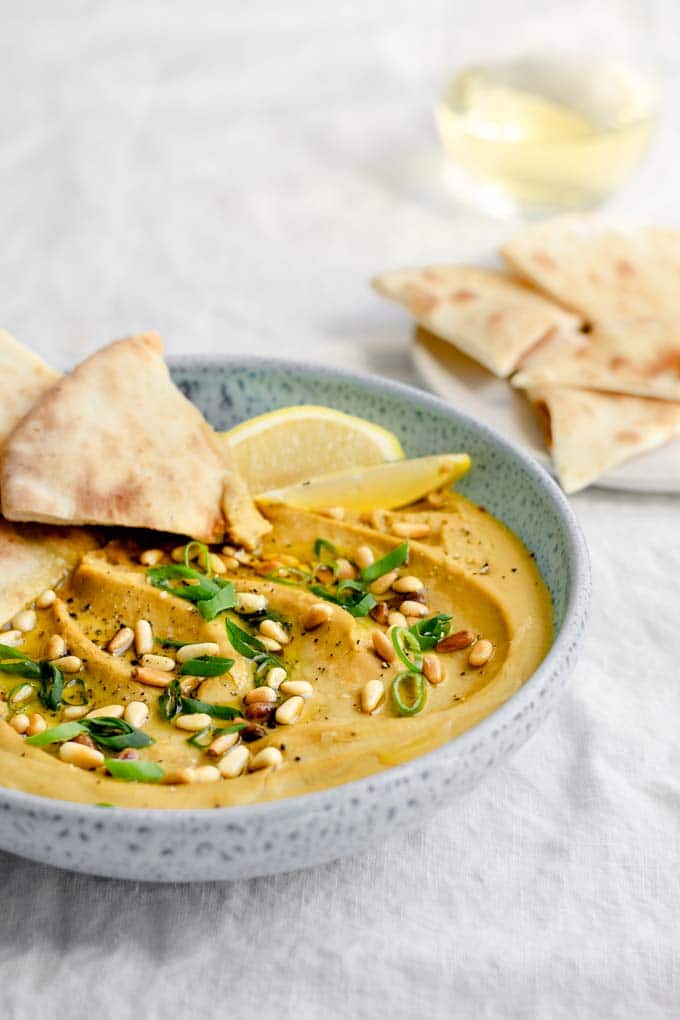 side view of the creamy favosalata with pine nuts and scallions for garnish and a plate of naan for dipping