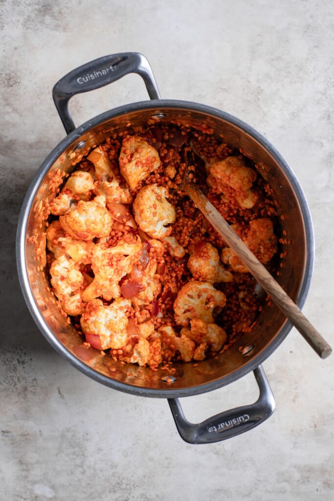 coliflor y lentejas rojas mezcladas en una olla con cebolla y curry rojo