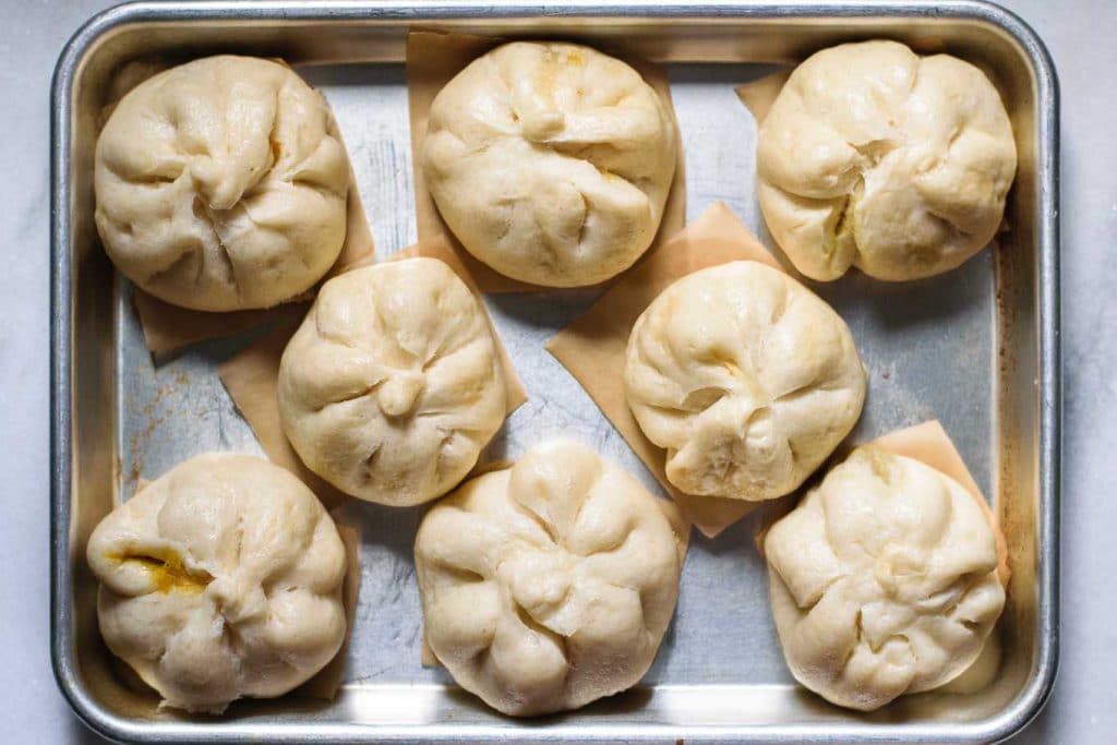steamed curry buns on individual parchment squares and on a baking tray, after steaming