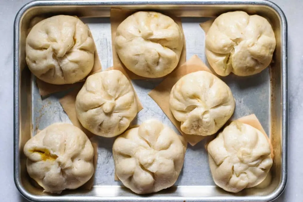 steamed curry buns on individual parchment squares and on a baking tray, after steaming