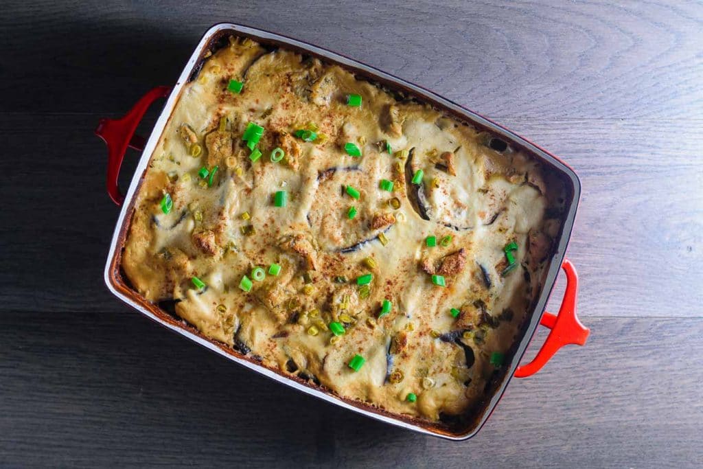 the vegan cheesy eggplant casserole in a red baking dish on a wooden background