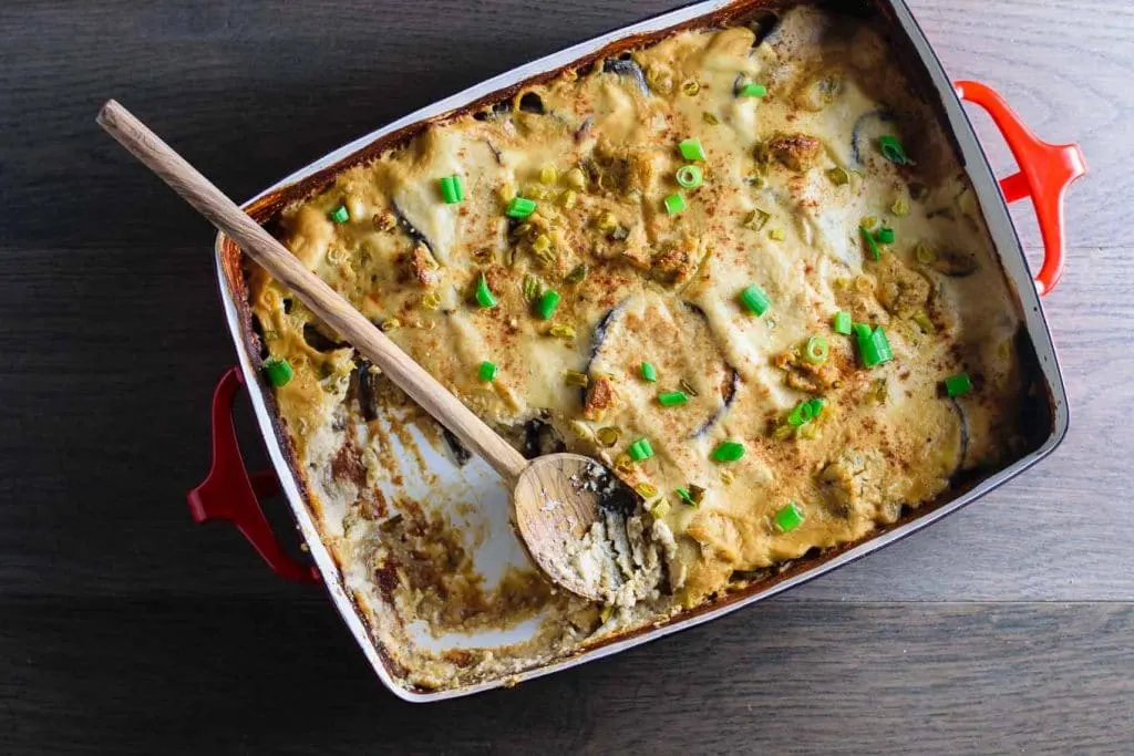 a wooden spoon in the vegan cheesy eggplant casserole dish, with a serving taken out, shot from above