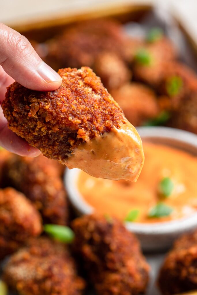 close up of vegan tempeh wing dipped into gochujang mayo