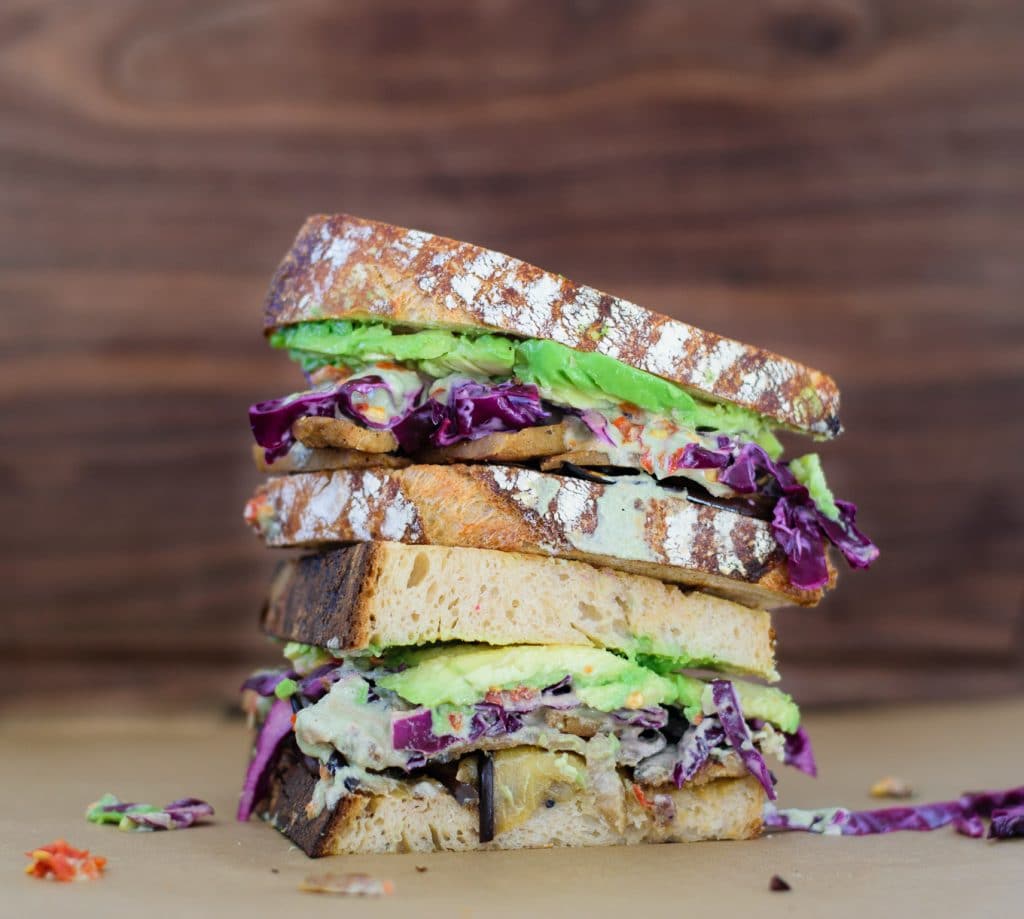 sandwich with madras marinated eggplant, seitan, cabbage slaw, pepita cream, chile sauce, and avocado on homemade toasted sourdough