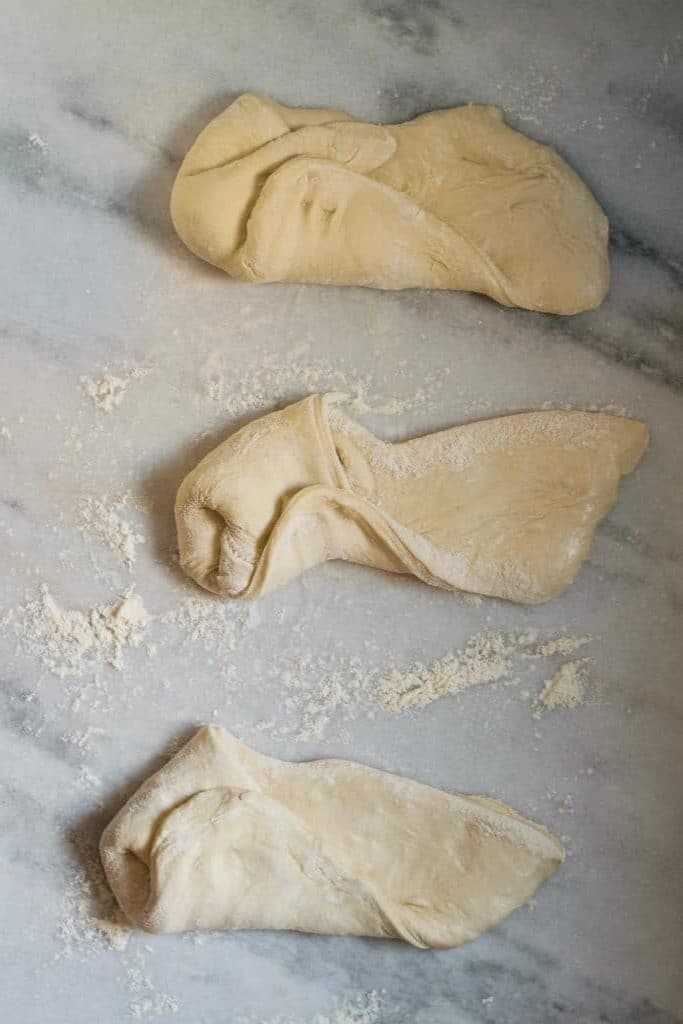 shaping the pizza dough into dough balls by stretching and folding the dough into the center