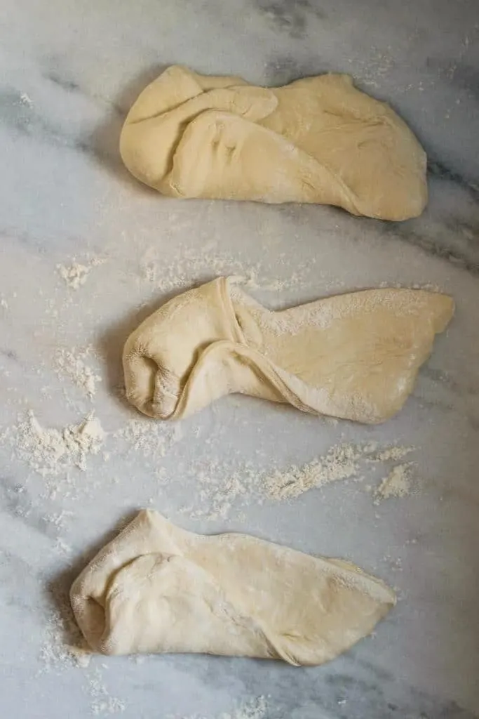 shaping the pizza dough into dough balls by stretching and folding the dough into the center