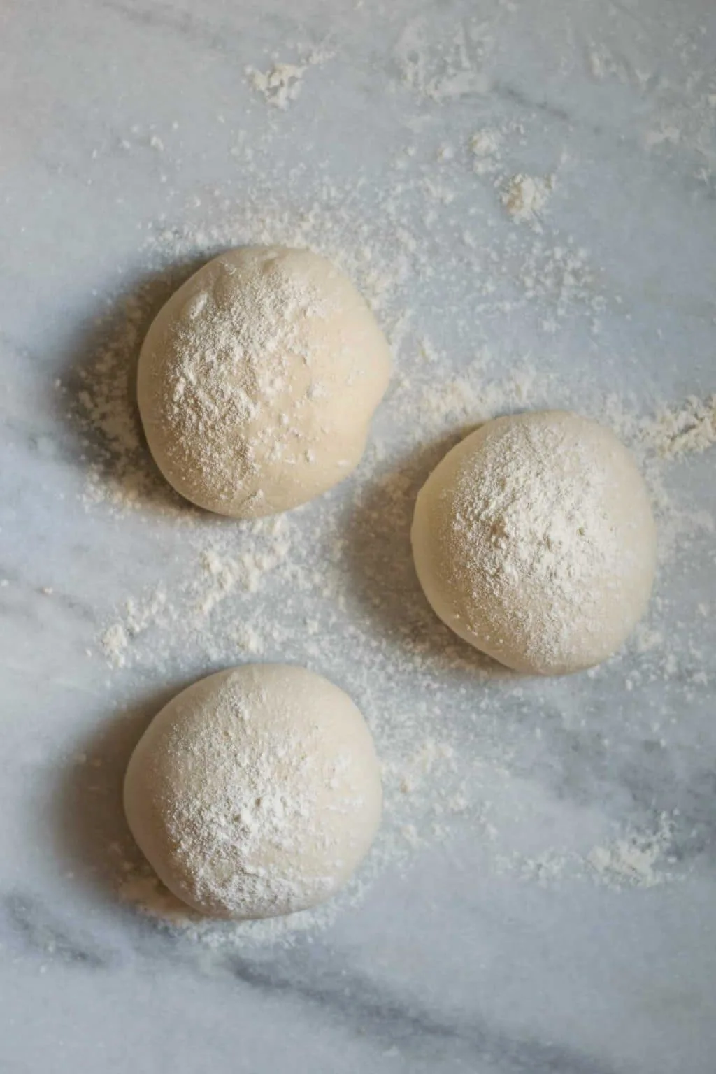 three shaped and floured dough balls on a marble counter