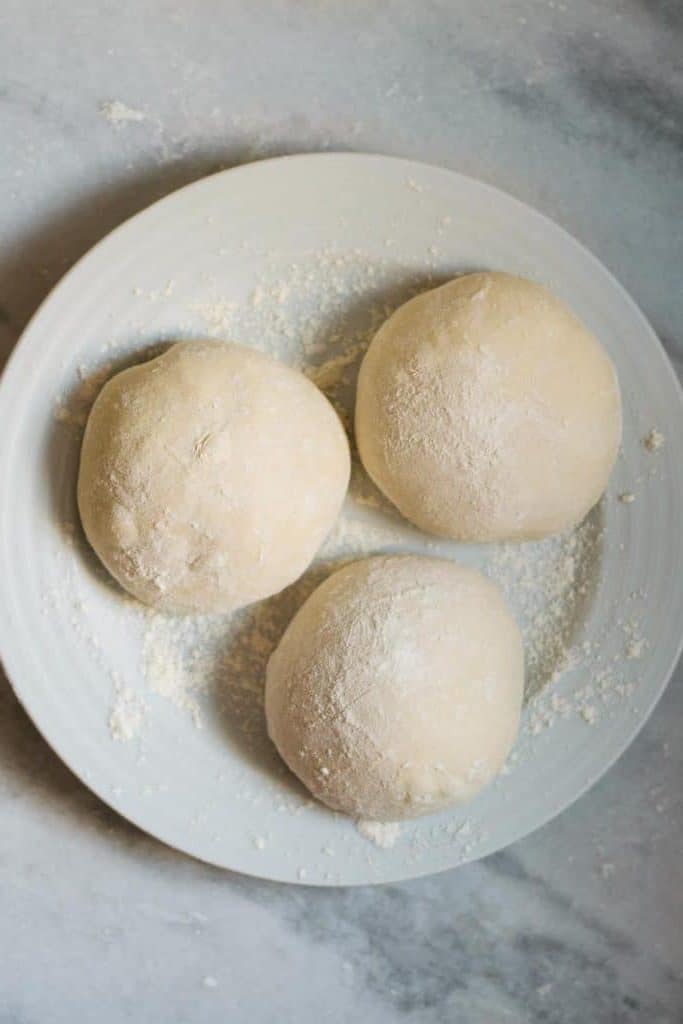 pizza dough balls shaped and sitting on a flour dusted plate, ready to be refrigerated