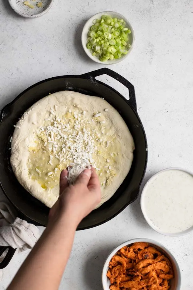 sprinkling vegan mozzarella onto pizza dough