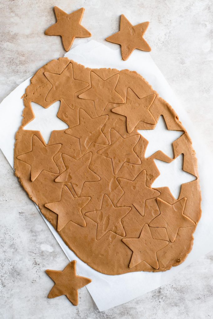 cookie dough rolled out and cut into star shaped with three removed from the rest of the dough