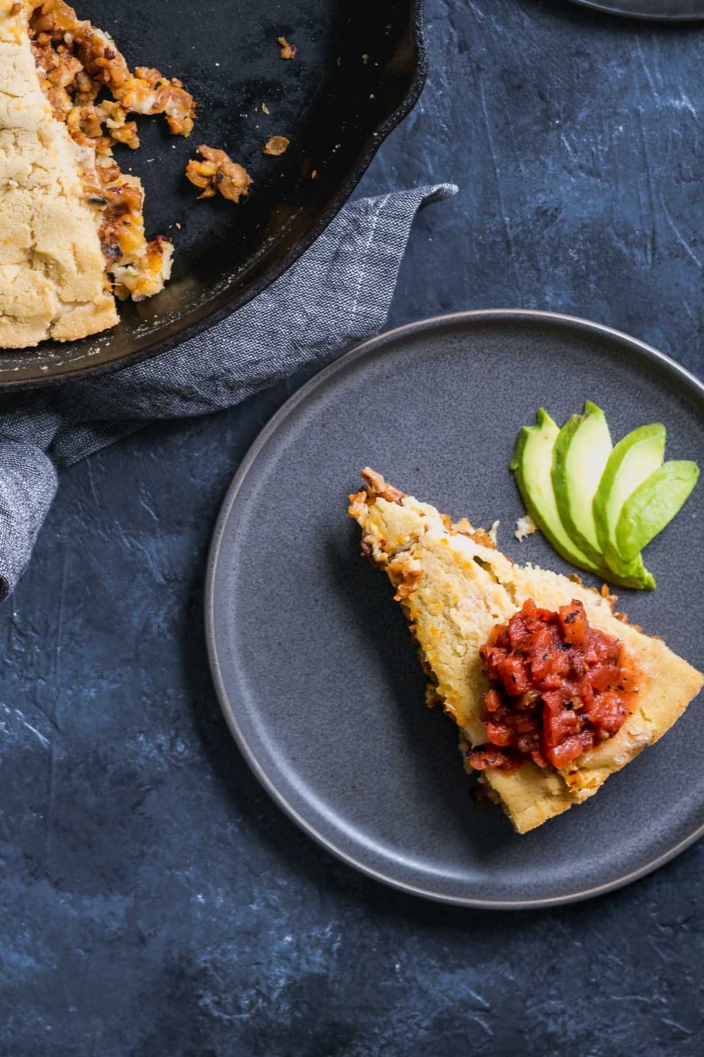 Slice of tamale skillet pie served on a plate with avocado and some tomato salsa