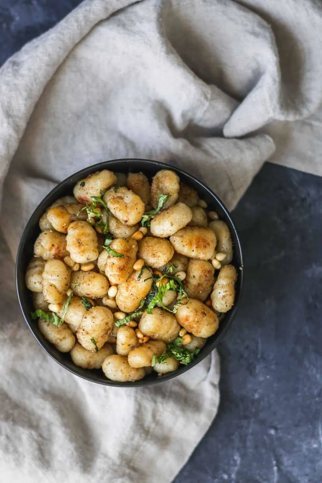 Vegan brown butter gnocchi in a black bowl over a tan towel