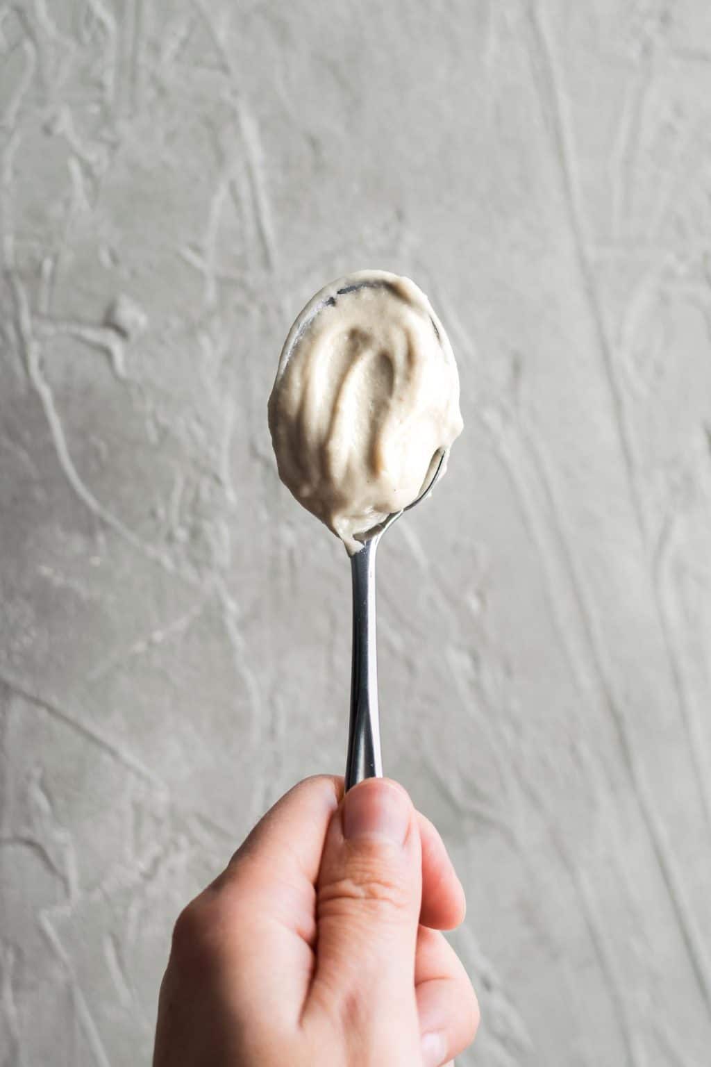 Thick and creamy vegan garlic white sauce on spoon