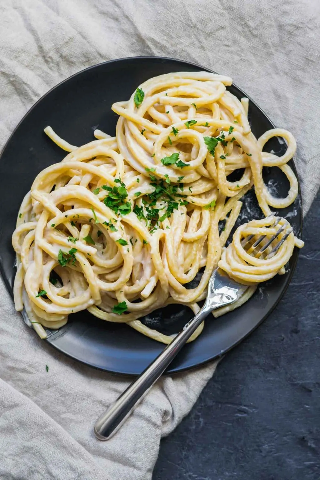 Thick and creamy vegan garlic white sauce is tossed with bucatini and garnished with minced parsley.