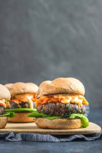 Vegan gochujang bean burgers are topped with butter lettuce, kimchi, fermented carrots, and gochujang mayo with a wheat bun.