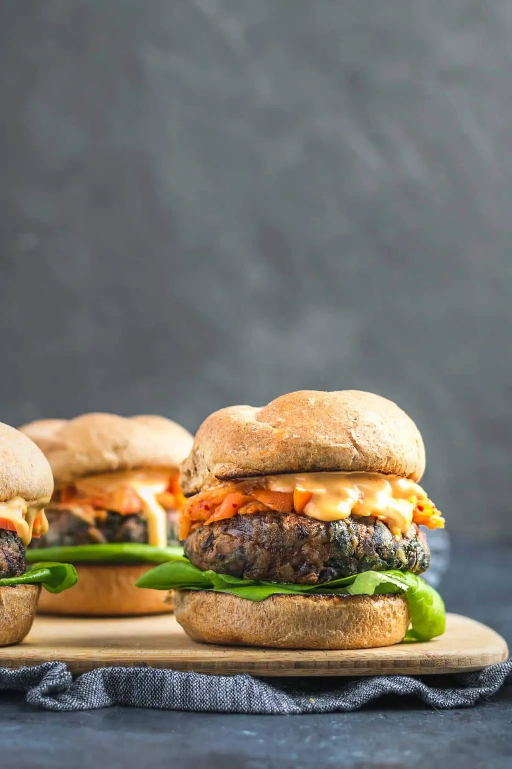 Vegan gochujang bean burgers are topped with butter lettuce, kimchi, fermented carrots, and gochujang mayo with a wheat bun.