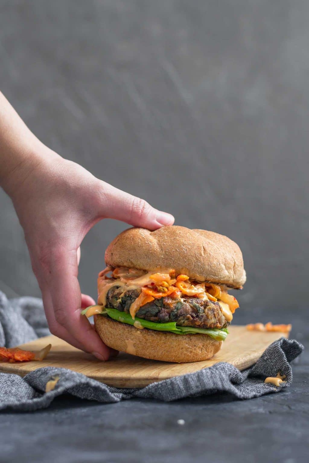 Vegan gochujang bean burgers topped with kimchi, fermented carrots, and gochujang mayo with a wheat bun.