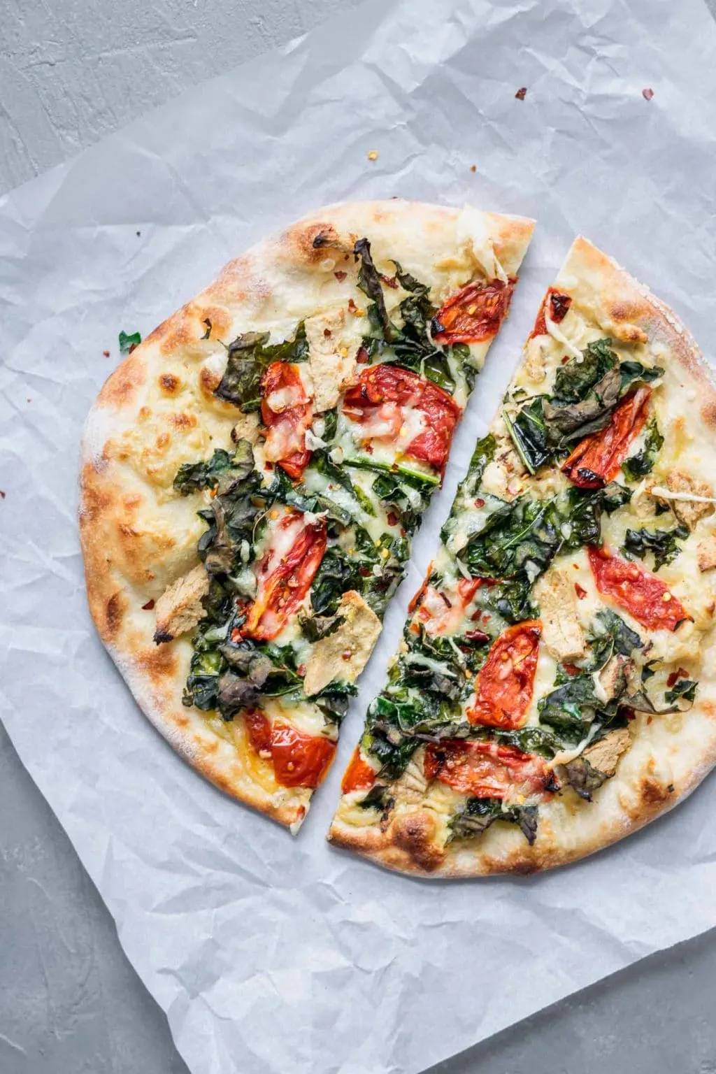 Crispy kale, roasted tomato, and vegan chicken white sauce pizza cut in half