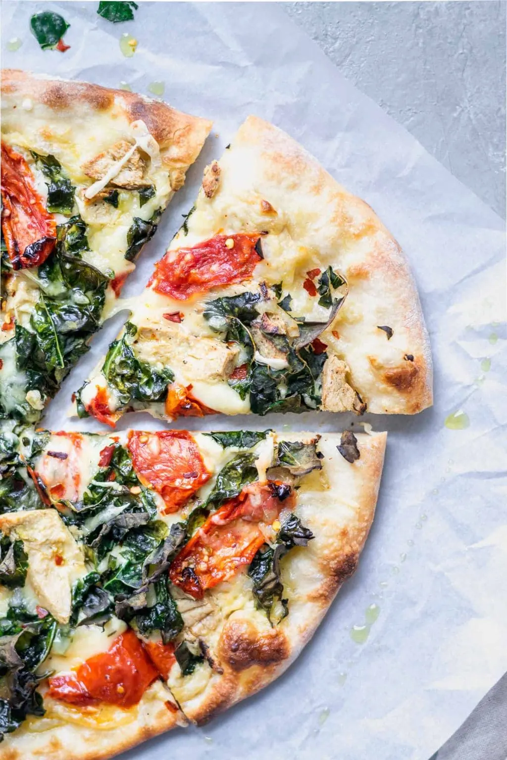 Slice of crispy kale, roasted tomato, and vegan chicken white sauce pizza