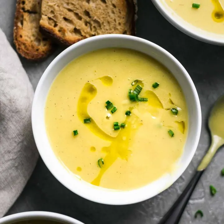 Vegan potato leek soup garnishes with a swirl of olive oil and minced chives and served with garlic bread