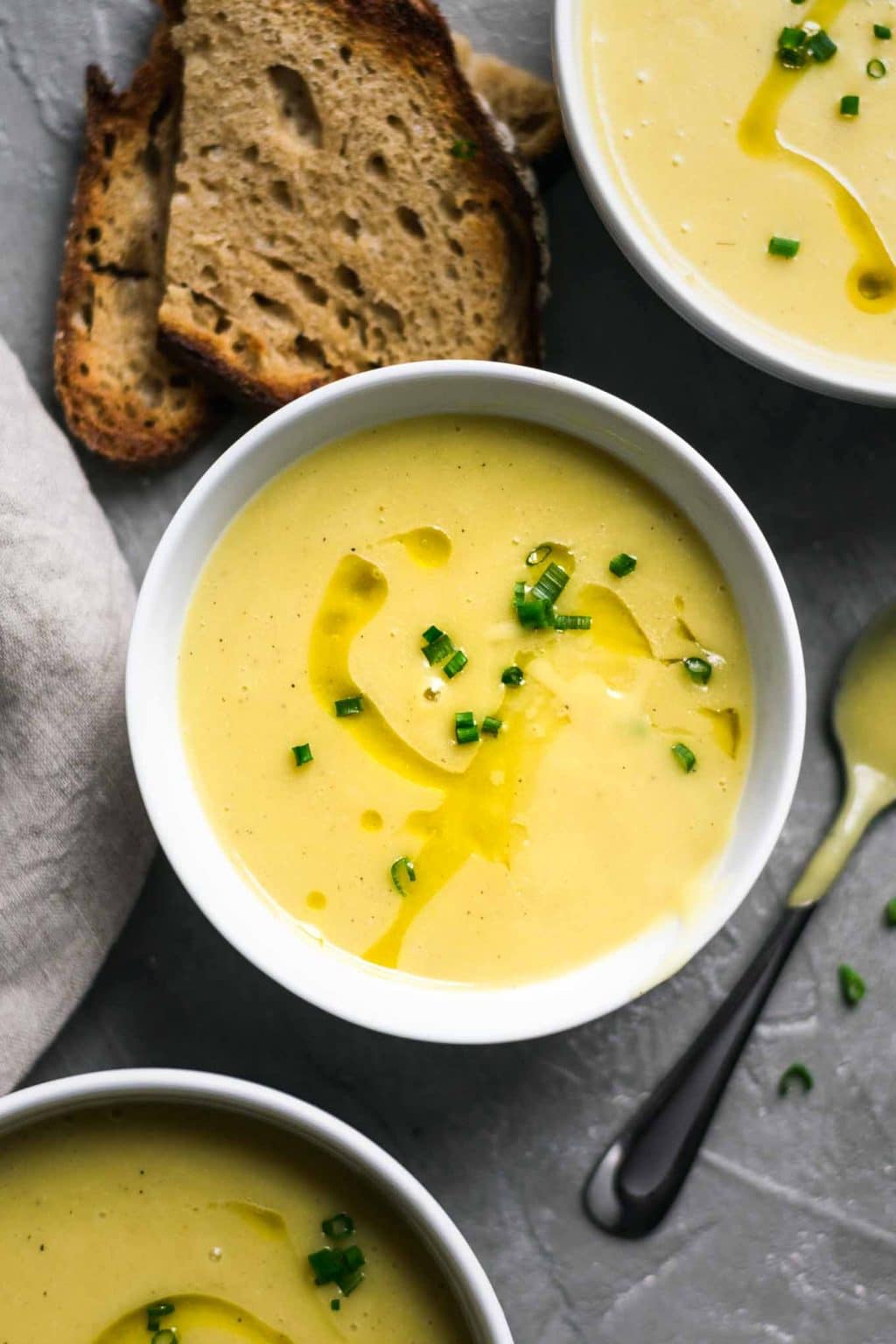 Vegan potato leek soup garnishes with a swirl of olive oil and minced chives and served with garlic bread