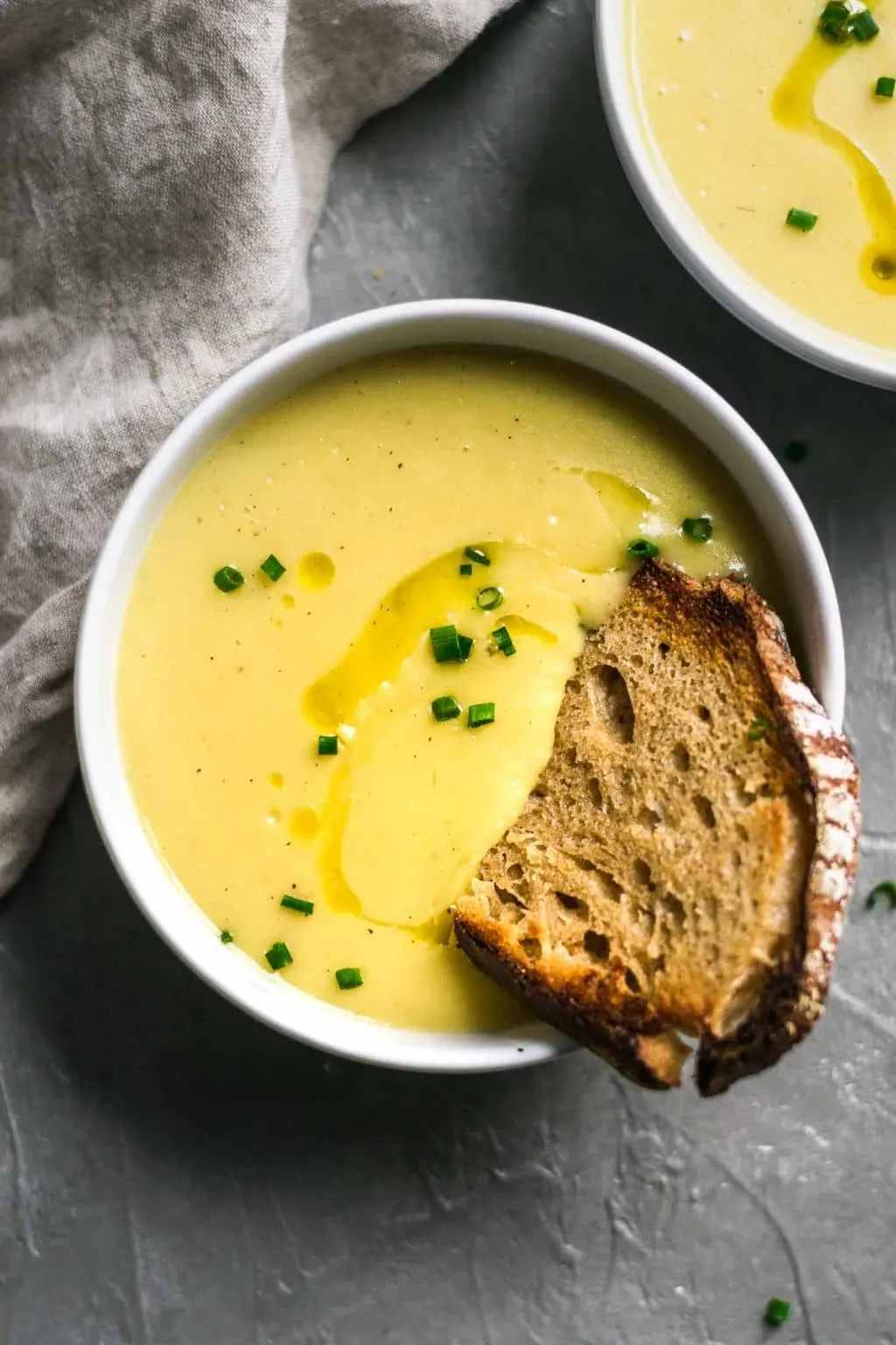 Vegan potato leek soup garnishes with a swirl of olive oil and minced chives and served with garlic bread