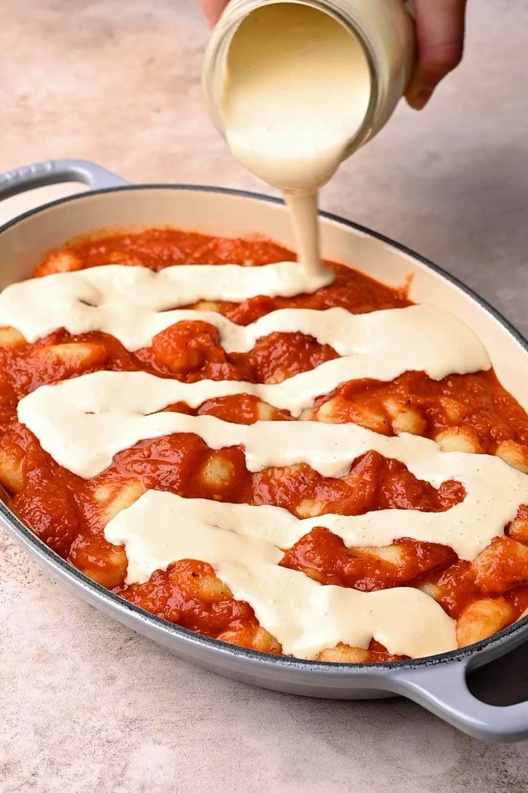 pouring mozzarella sauce over the gnocchi