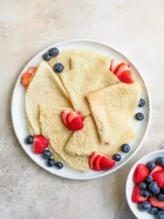vegan crepes folded into quarters and served with fresh sliced strawberries and blueberries