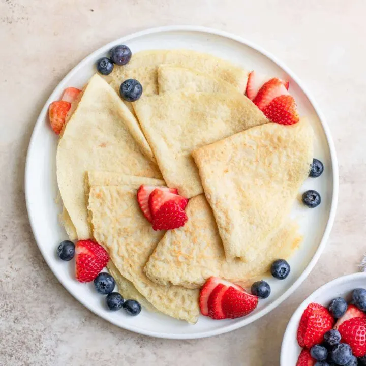 vegan crepes folded into quarters and served with fresh sliced strawberries and blueberries