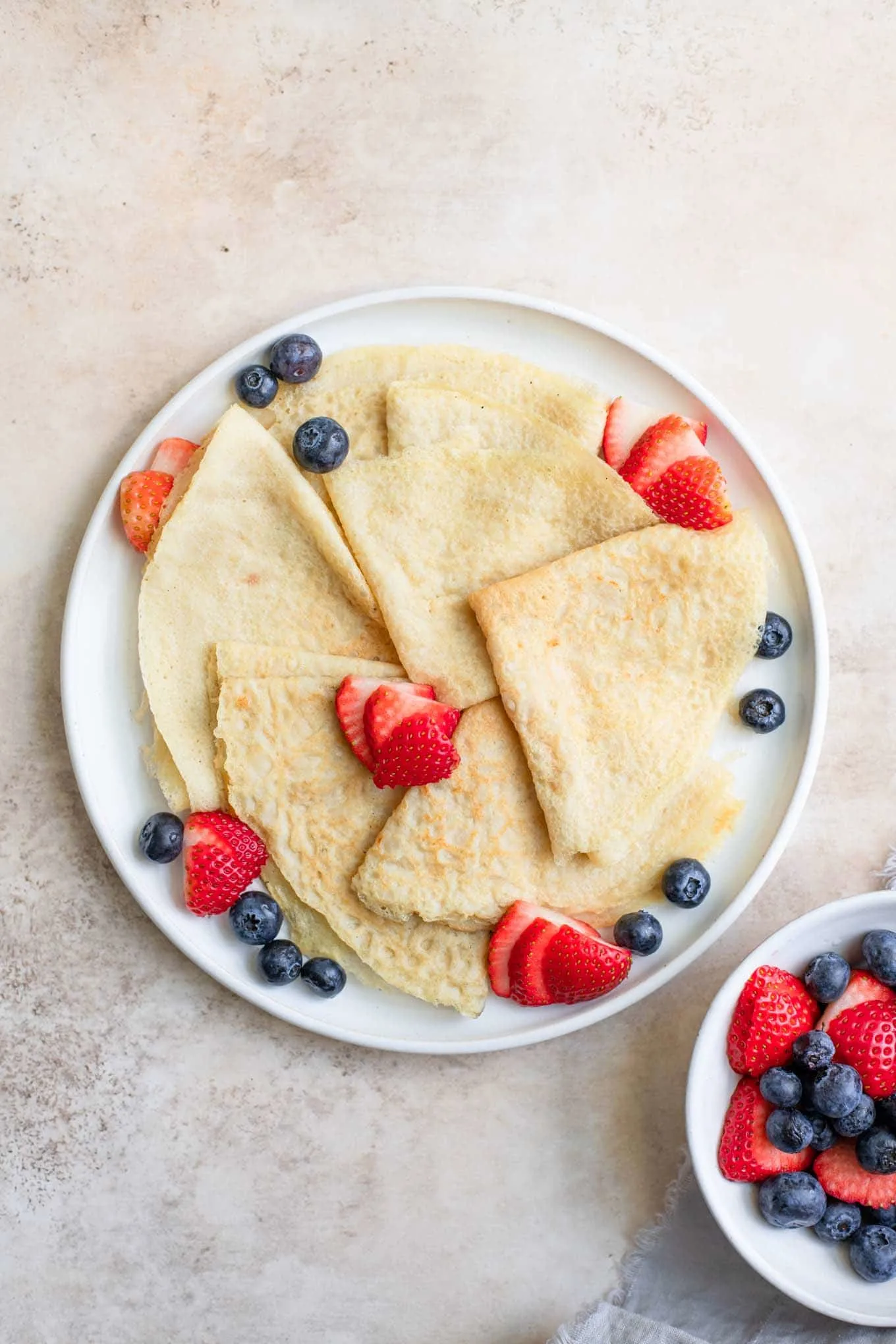 vegan crepes folded into quarters and served with fresh sliced strawberries and blueberries