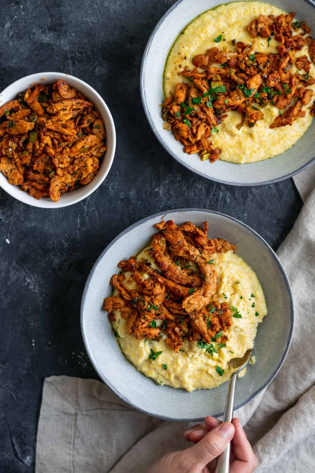 Cajun soy curls and creamy vegan jalapeño grits, 2 bowls with a fork taking a scoop of grits out of the bottom bowl and an extra bowl of cajun soy curls