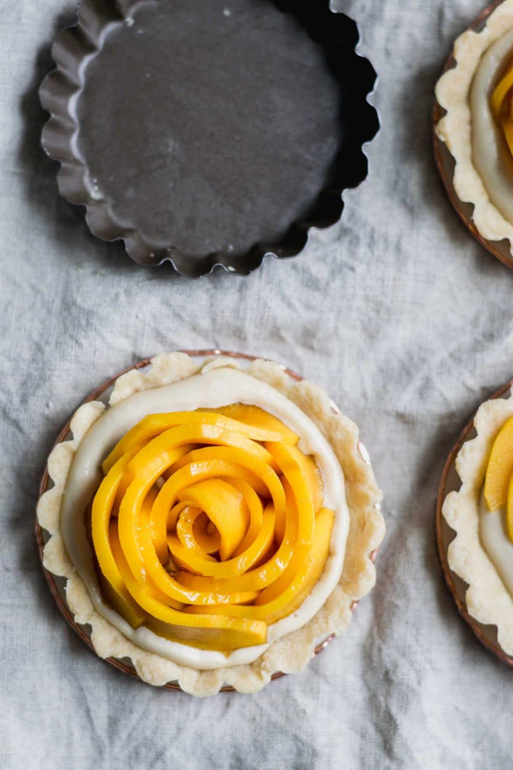 vegan mango tarts with vanilla pastry cream and shortbread crust. Mangoes are cut into rosettes.