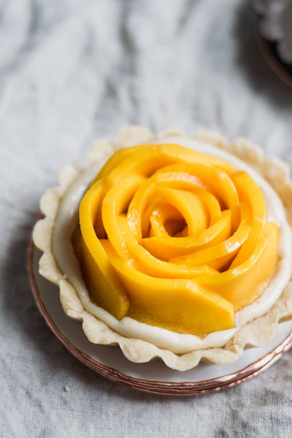 vegan mango tarts with vanilla pastry cream and shortbread crust. Mangoes are cut into rosettes.