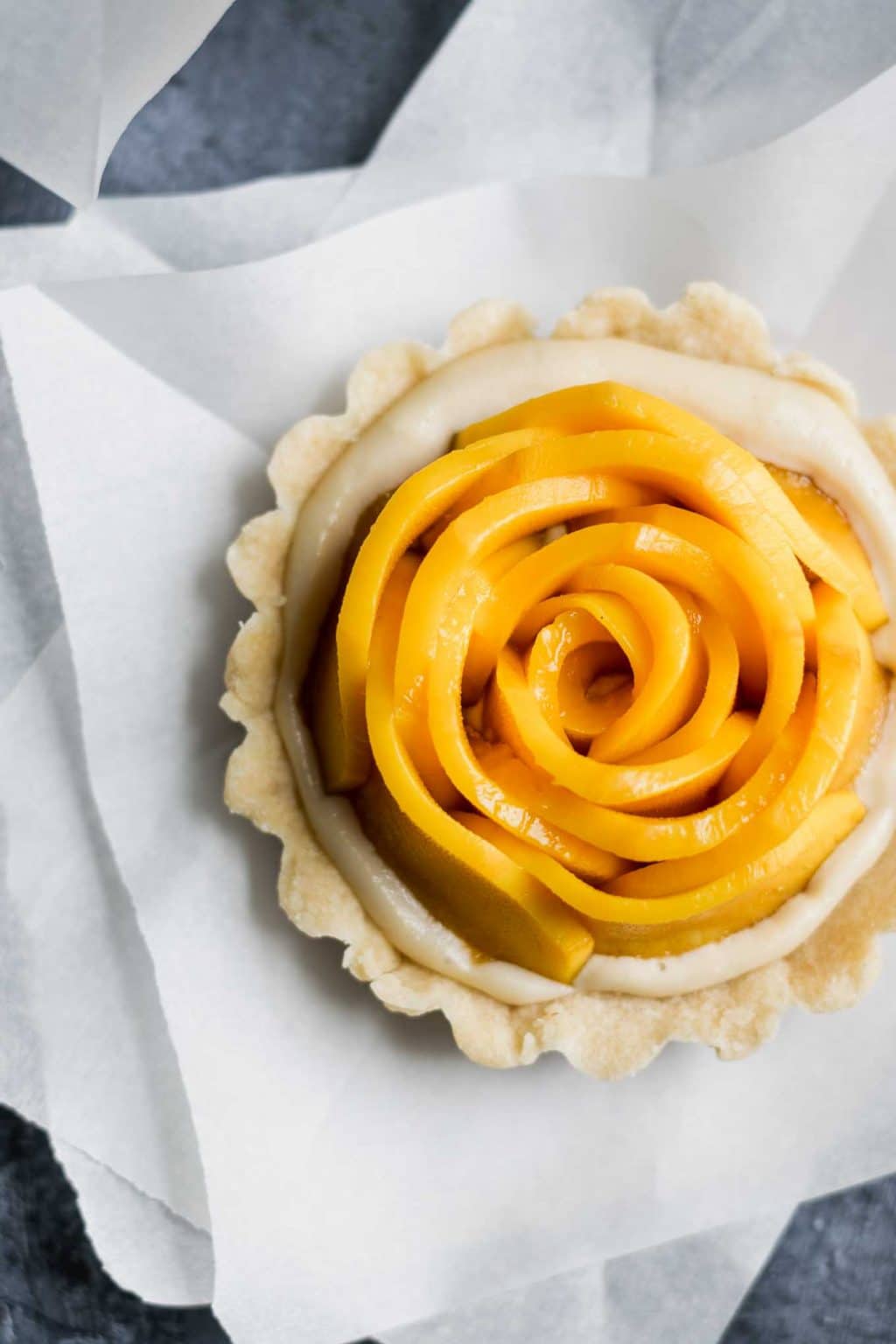 vegan mango tarts with vanilla pastry cream and shortbread crust. Mangoes are cut into rosettes.