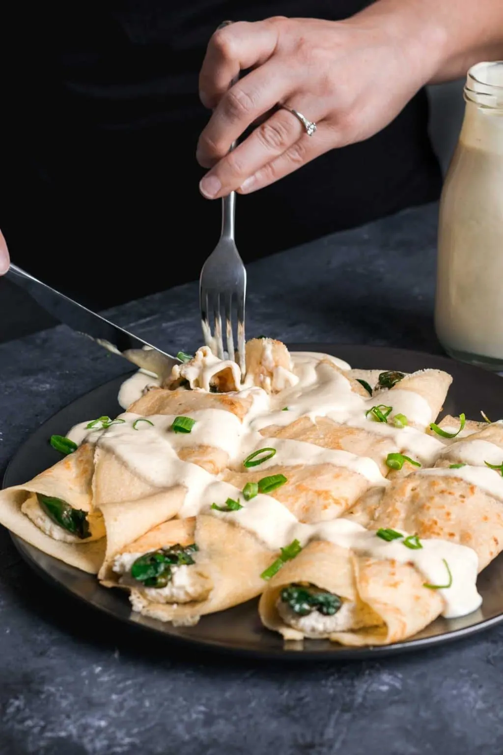 Cutting into savory crepes stuffed with almond cheese and sauteed spinach with vegan hollandaise drizzled on top. Garnished with scallion greens.