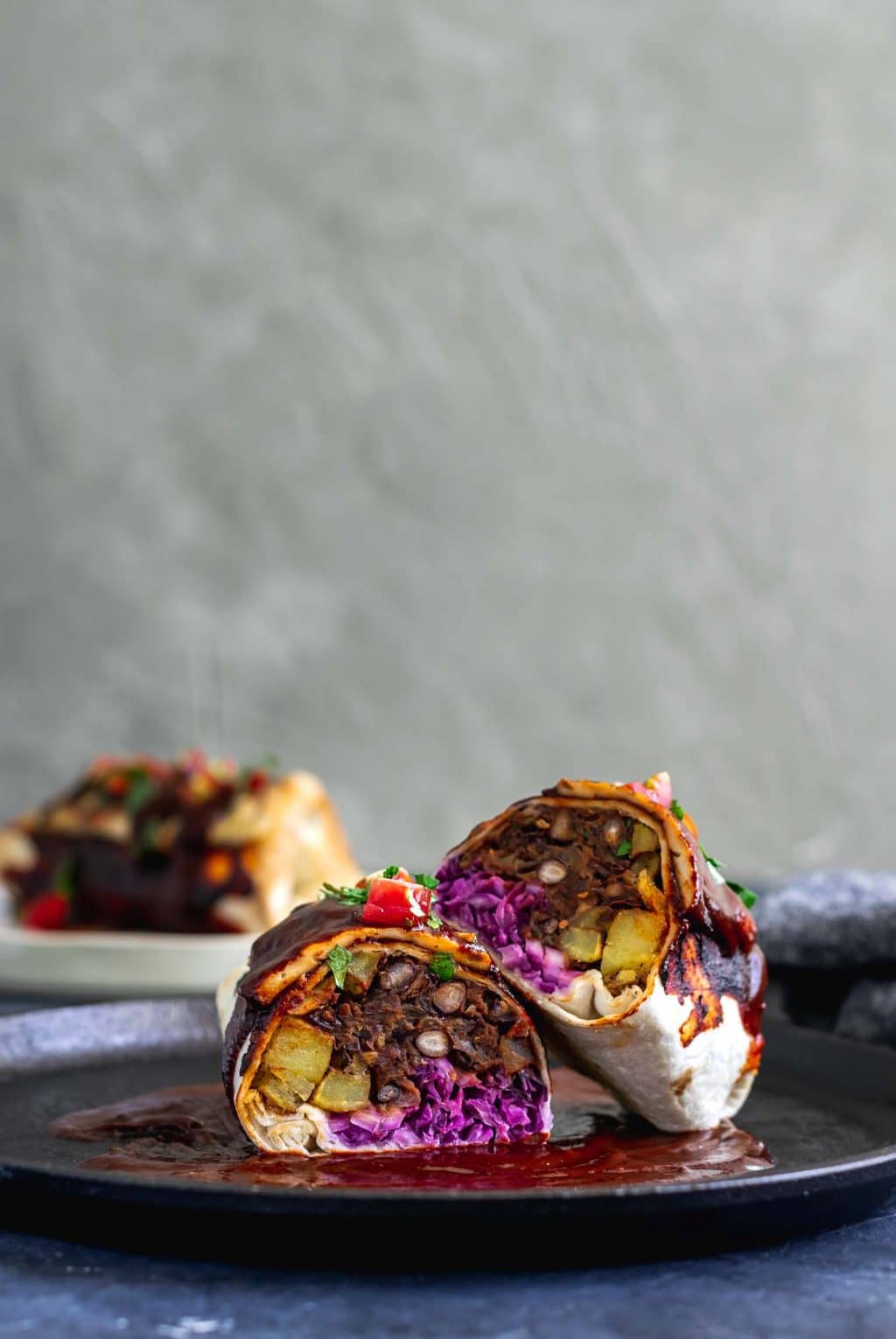 Vegan smothered burritos with red sauce cut open to show the black bean, potato, and cabbage slaw filling